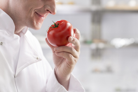 Midsection of mature chef smelling fresh red tomato while standing at restaurant kitchenの写真素材