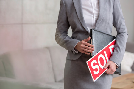 Midsection of young saleswoman holding sold placard and document in apartmentの写真素材