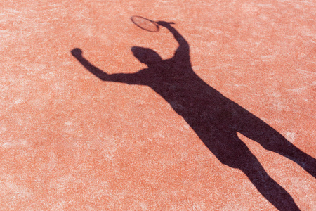 Shadow of successful man standing with arms raised on red tennis court during matchの写真素材