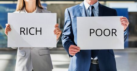 Man and woman holding white placard with RICH and POOR signの写真素材