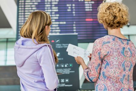 Portrait of mother and daughter looking at flights on monitor in airportの写真素材