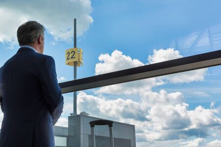 Portrait of mature businessman standing with his suitcase while looking through the window in airportの写真素材