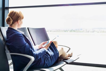 Young beautiful airport staff using digital tablet while sitting on chair during breakの写真素材