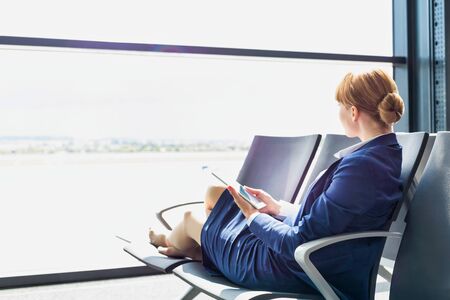 Young beautiful airport staff using digital tablet while sitting on chair during breakの写真素材