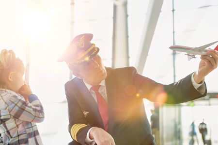 Portrait of mature pilot holding airplane toy while playing with cute little girl in airportの写真素材