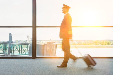 Portrait of mature pilot walking in airport with yellow lens flareの写真素材