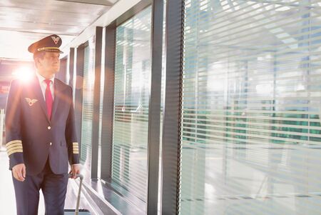 Portrait of mature pilot walking with his suitcase in airportの写真素材