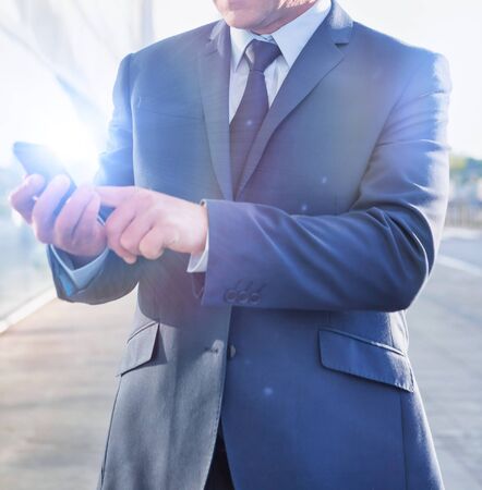 Portrait of mature businessman using smartphone in airport with lens flareの写真素材