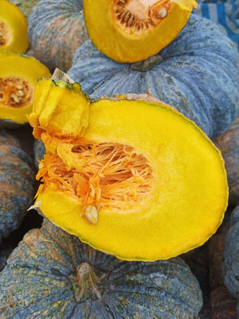 Fresh pumpkin cut open to show yellow interior in background of heap of pumpkins in vegetable market for saleの写真素材