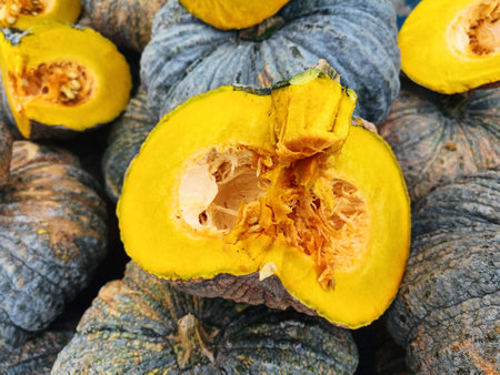 Fresh pumpkin cut open to show yellow interior in background of heap of pumpkins in vegetable market for saleの写真素材