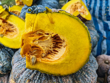 Fresh pumpkin cut open to show yellow interior in background of heap of pumpkins in vegetable market for saleの写真素材