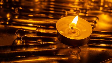 A romantic melting candle with orange flame on the glass and metal floor. Faith and romance concept....