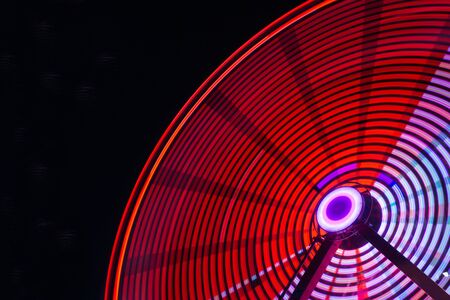 A part of colorful bright ferris wheel at night capture with long exposure. Red and white neon light motion on dark sky background.の写真素材