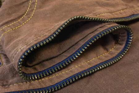 A close up of curvy golden zip teeth track on the brown denim fabric