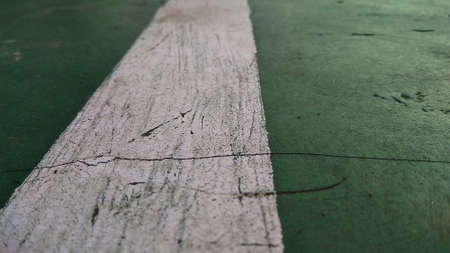 Close up of a chapped-white line drawn on a green-broken floor at public sports field.