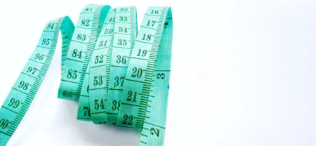 Old wrinkled green rubber tape measure with negative space. Rubber tape measure isolated on the gray white background. Useful for sewing cloth or fabric.の写真素材