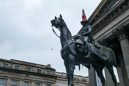 Statue of Duke of Wellington, riding a horse, wearing a traffic cone on his head. In front of...