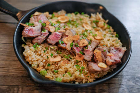 Beef with garlic fried rice, a Japanese dish consisting of a bowl of rice topped with rare beef served on a black panの写真素材