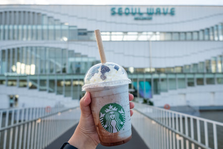Seoul, South Korea - 14 July 2022: Hand holding cup of Mint Chocolate Cip blended in front of Seoul Wave Art Center building, floating Starbucks on Hangang or Han River.のeditorial素材