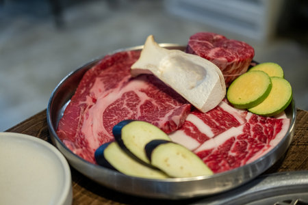 A close-up shot of premium cuts of marbled Hanwoo beef placed on a metal tray, with sliced eggplant and zucchini and eryngii mushroomの写真素材