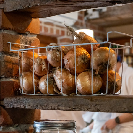 A basket of onions stored on a wooden shelf against a brick wallの写真素材