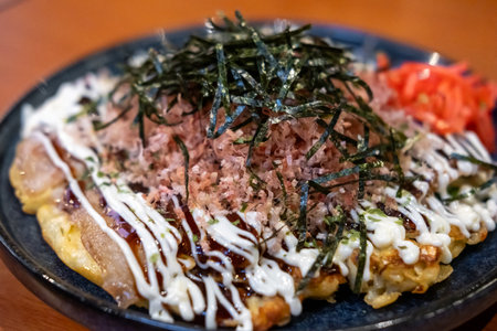 Okonomiyaki, a Japanese pizza or pancake containing a variety of ingredients served on plate with dried seaweed and dried bonito flakesの写真素材