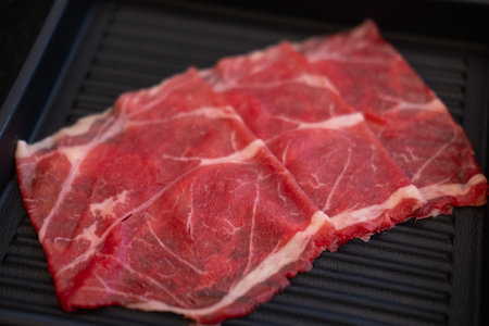 A close-up shot of sliced raw meat, arranged on a plate, ready to be cooked in a hot potの写真素材
