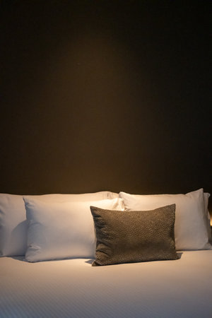 A neatly made hotel bed with soft pillows with warm reading lightの写真素材