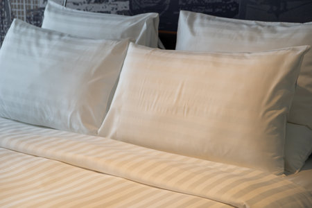 A neatly made hotel bed with soft pillows with warm reading lightの写真素材