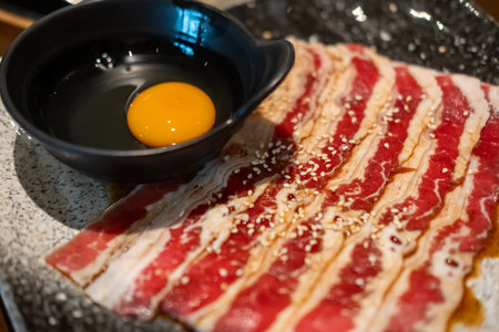 Close up of sliced meat, with a bowl of raw egg.の写真素材