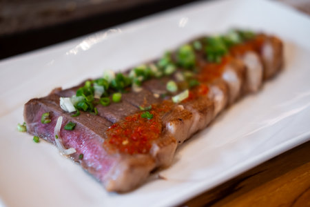 Japanese sliced medium rare steak served on plate, topped with sliced spring onion and sauceの写真素材
