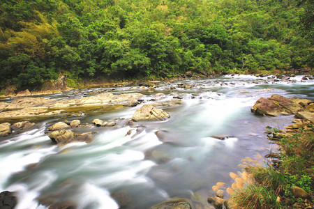 Beautiful flowing river scenery with rocks and trees among the mountainsの写真素材