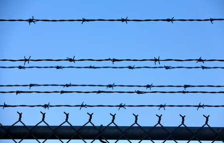 Barbed wire fence on blue sky background. Close-up.の写真素材