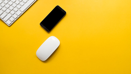 Office desk table with keyboard and mouse with smartphone top view on yellow background