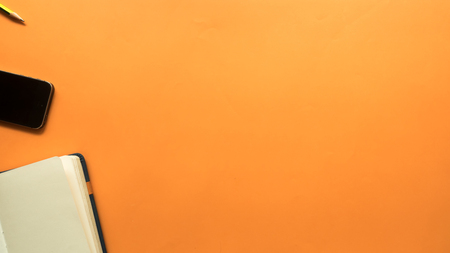 workspace desk with smarth phone and notebook copy space orange backgroundの写真素材