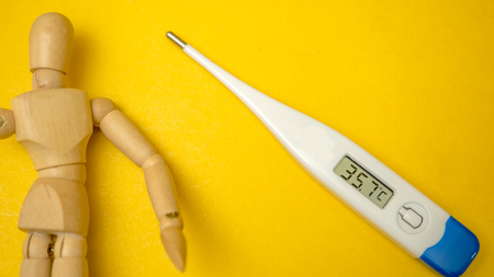 Electronic modern thermometer with wooden dummy on yellow background.Close up