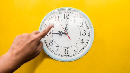 Clock with hand on yellow background