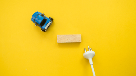 The electric car is connected by a wire with a plug from the socket and wood block. Sign symbol
