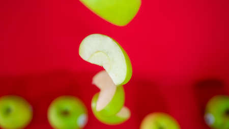 Fresh flying green apple cut with drop of water isolated on red backgroundの写真素材