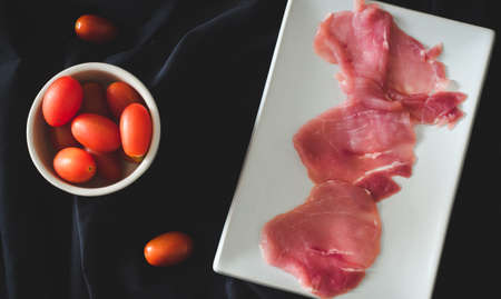 Miniature tomatoes and  raw meat on black backgroundの写真素材