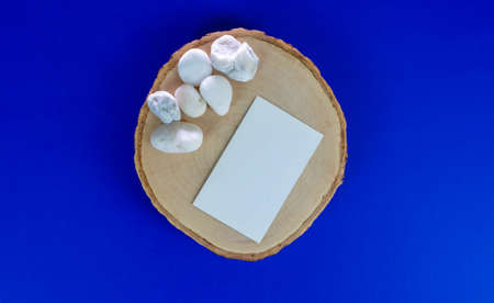 stationery mock-up scene. Blank white card, wooden plate, blue background and white stone. Feminine flat lay, top view.の写真素材