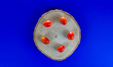 Red tiny tomatoes on a wooden cutting board on blue backgroundの写真素材