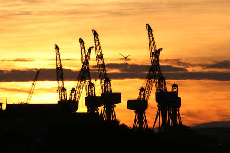 The cranes of a Clyde shipyard silhouetted by a Glasgow sunsetの写真素材