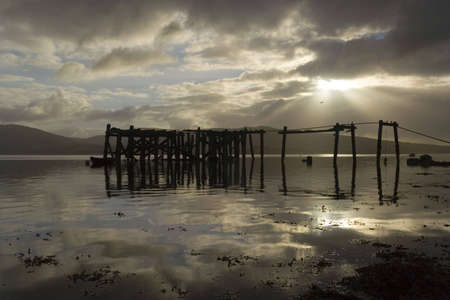 A ruined pier reflected in the calm of a morning seashoreの写真素材