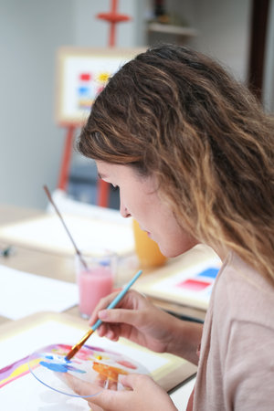 Close-up of a young woman painting with a brush with acrylic paints on paper. Painting training, drawing lesson in an art studio. Abstract drawing with acrylic paints during training.の写真素材