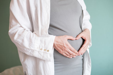 Pregnant woman with a big belly in the last month of pregnancy. The woman folding her hands in a heart shape over her pregnant belly. The love and care of a mother for her baby. Happy motherhood.の写真素材