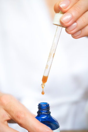 A close side shot of a blue bottle with serum, drops falling from a pipette. Close up shot of drops of moisturizing serum for skin. A product for middle-aged skin. Vertical photo.の写真素材
