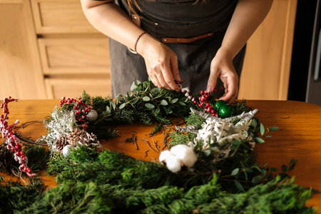 DIY decorations for the New Year. A making a Christmas wreath from fir branches. The hands of a young woman above the table collect a wreath and decorate it with cones and balls.の写真素材