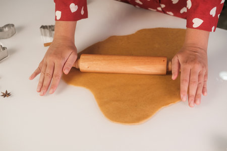 Close up of a young womans hands in red pajamas with hearts rolling out gingerbread dough with a...