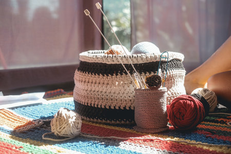 A close up of a knitted basket in which there are multi colored balls of wool threads, next to there is a glass with knitting needles and crochet hooks. Making knitted clothes. DIY plaid.の写真素材